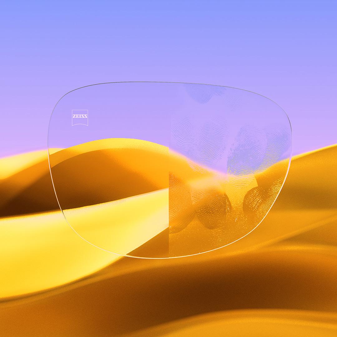 Et delt brilleglass der den ene siden er klar og ren med ZEISS DuraVision Gold UV, mens den andre siden et dekket av fingeravtrykk.