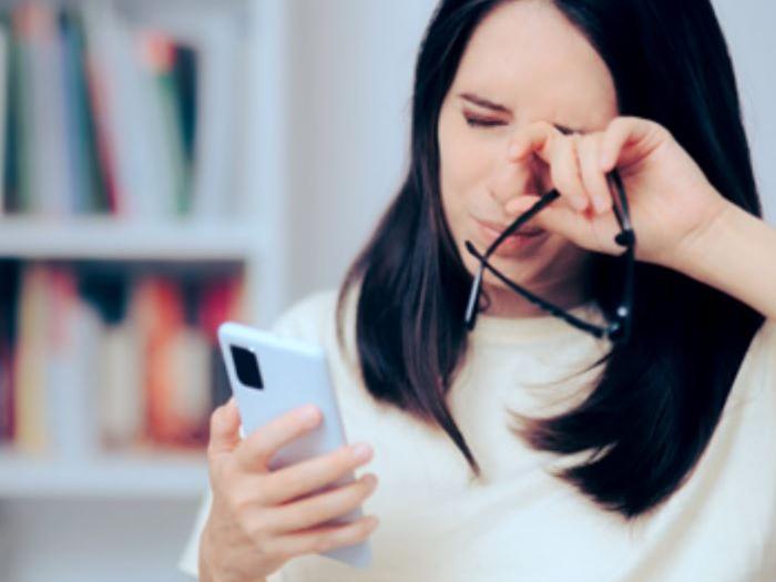 Et bilde som viser en kvinne i 30-årene som ser på telefonen mens hun gnir seg i øynene.
