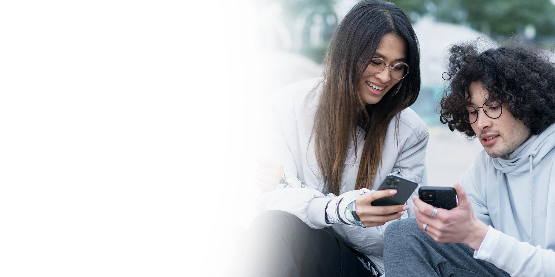 To unge mennesker, en kvinne med langt brunt hår som smiler og en gutt med krøllete svarte hår med ZEISS SmartLife-briller som ser på telefonene sine. 