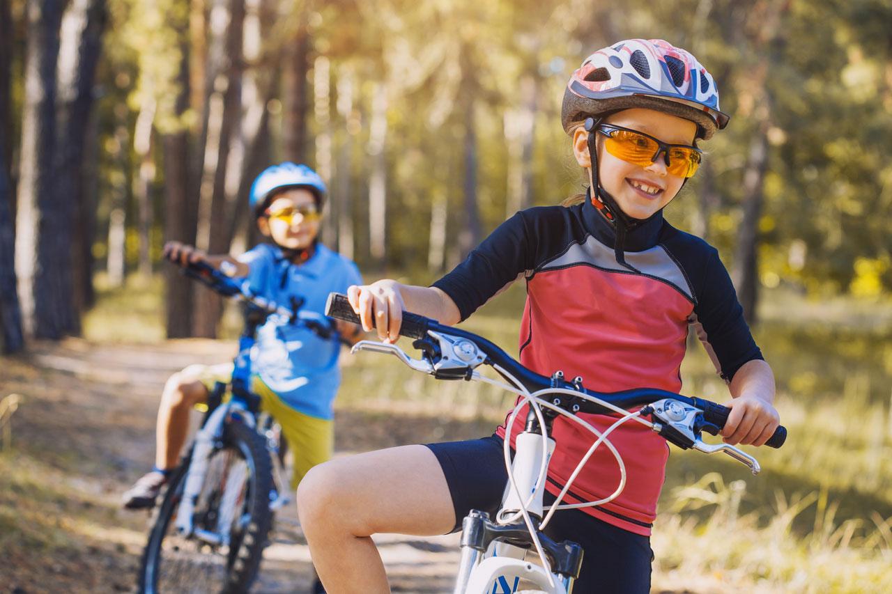 Barn på sykler i en solfylt skog Barn som sykler ute med hjelm