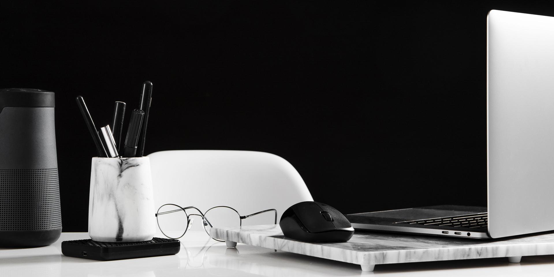 Ryddig arbeidsplass som viser en åpen bærbar datamaskin på høyre side med en mus. Foran den ligger et par briller. På venstre side av bildet er en boks med penner.