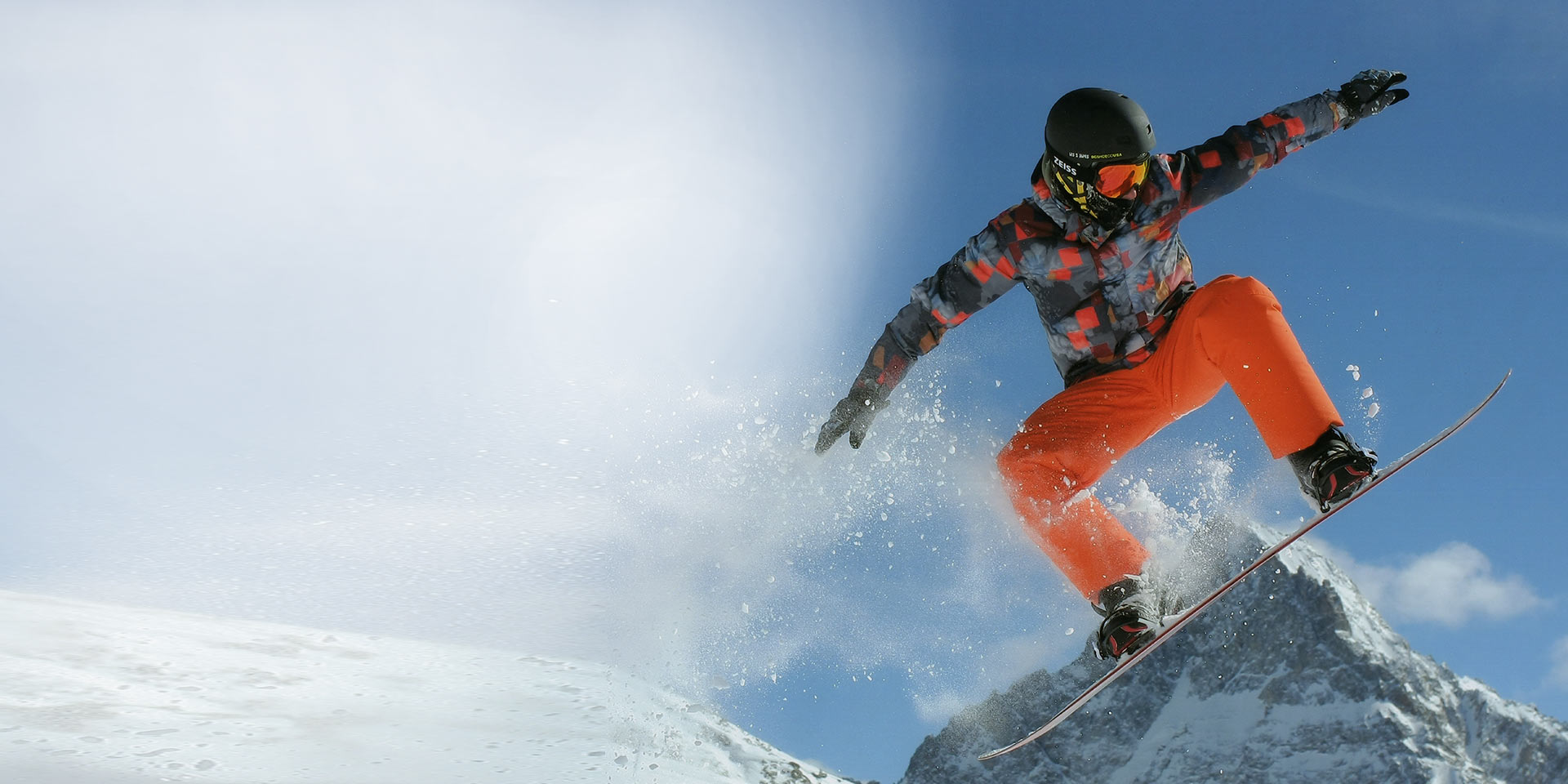 En mann hopper på snowboard. Han bruker en svart skihjelm og ZEISS skibriller med utskiftbar teknologi til beskyttelse