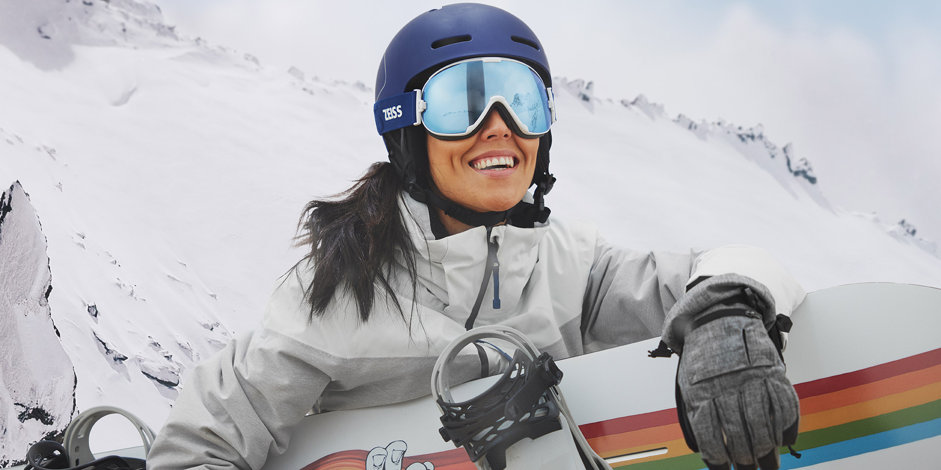 En ung kvinner bruker skibriller med ZEISS teknologi med utskiftbare glass og holder et snowboard.