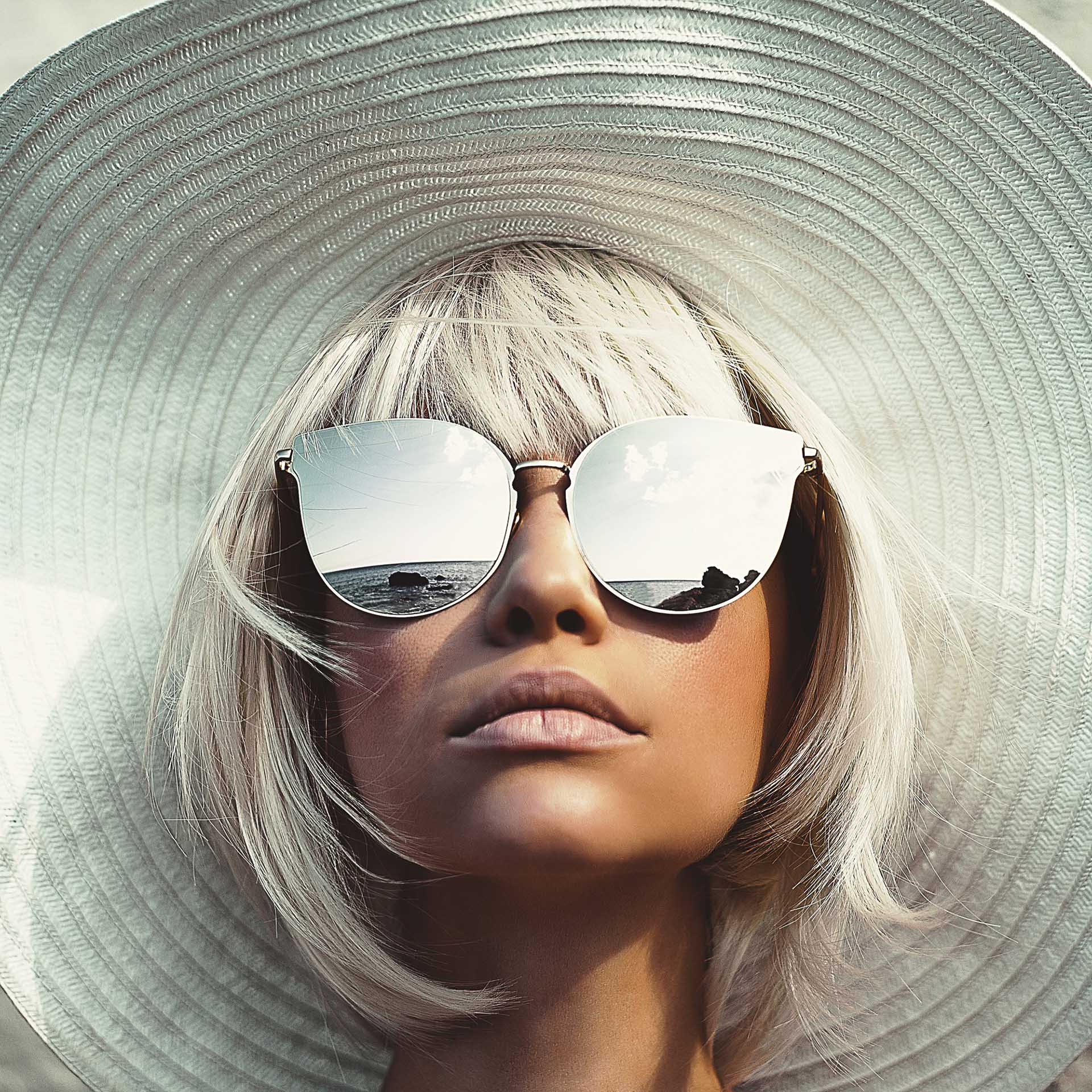 Ung kvinne med stor solhatt ser opp og har på seg store solbriller med speileffekt
