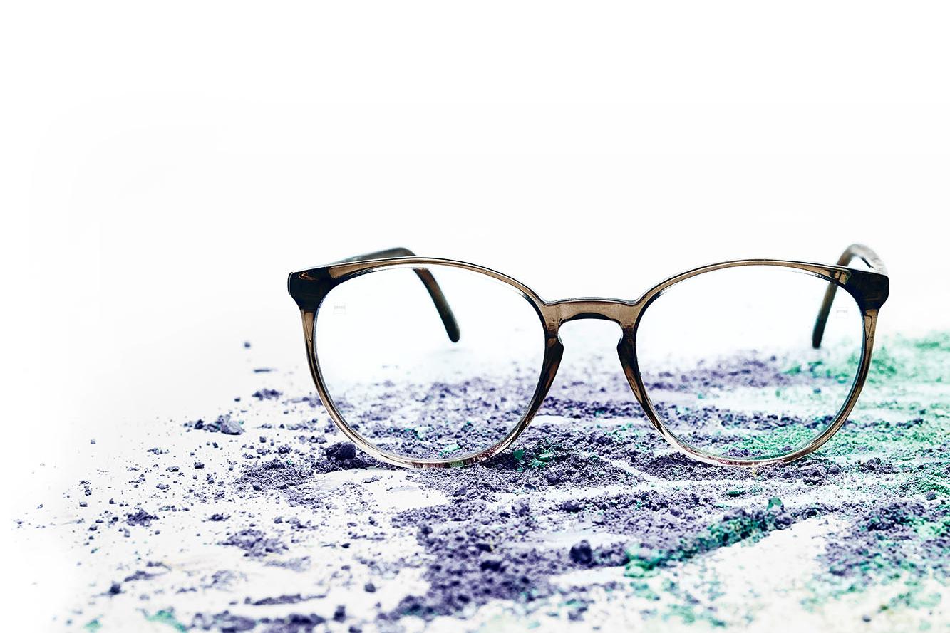 Et par briller med klare glass ligger på fargerikt pulver.