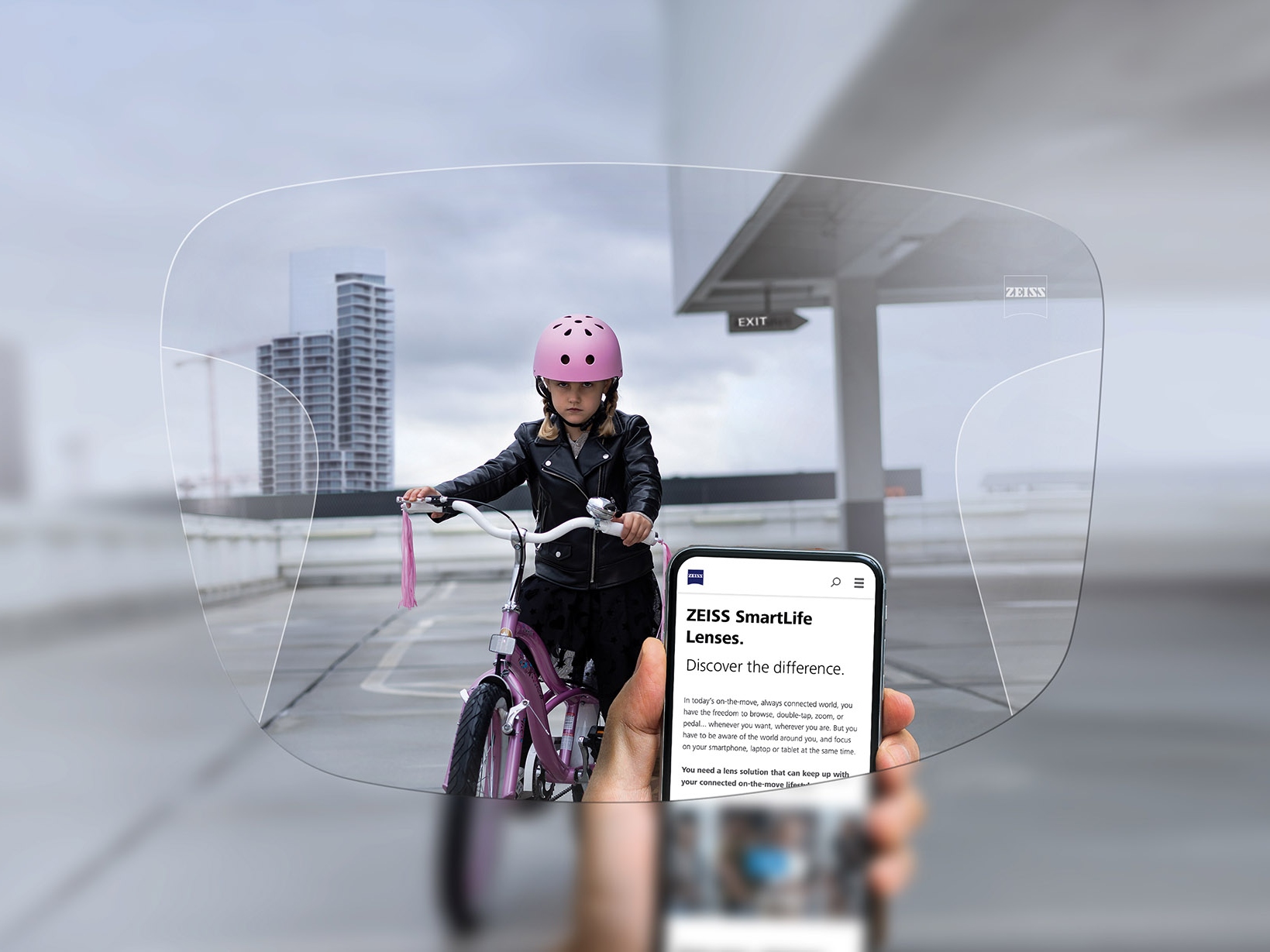 Person som ser på telefonen sin gjennom ZEISS SmartLife progressive glass. I bakgrunnen kan du se en jente på sykkelen med rosa styrthjelm. 