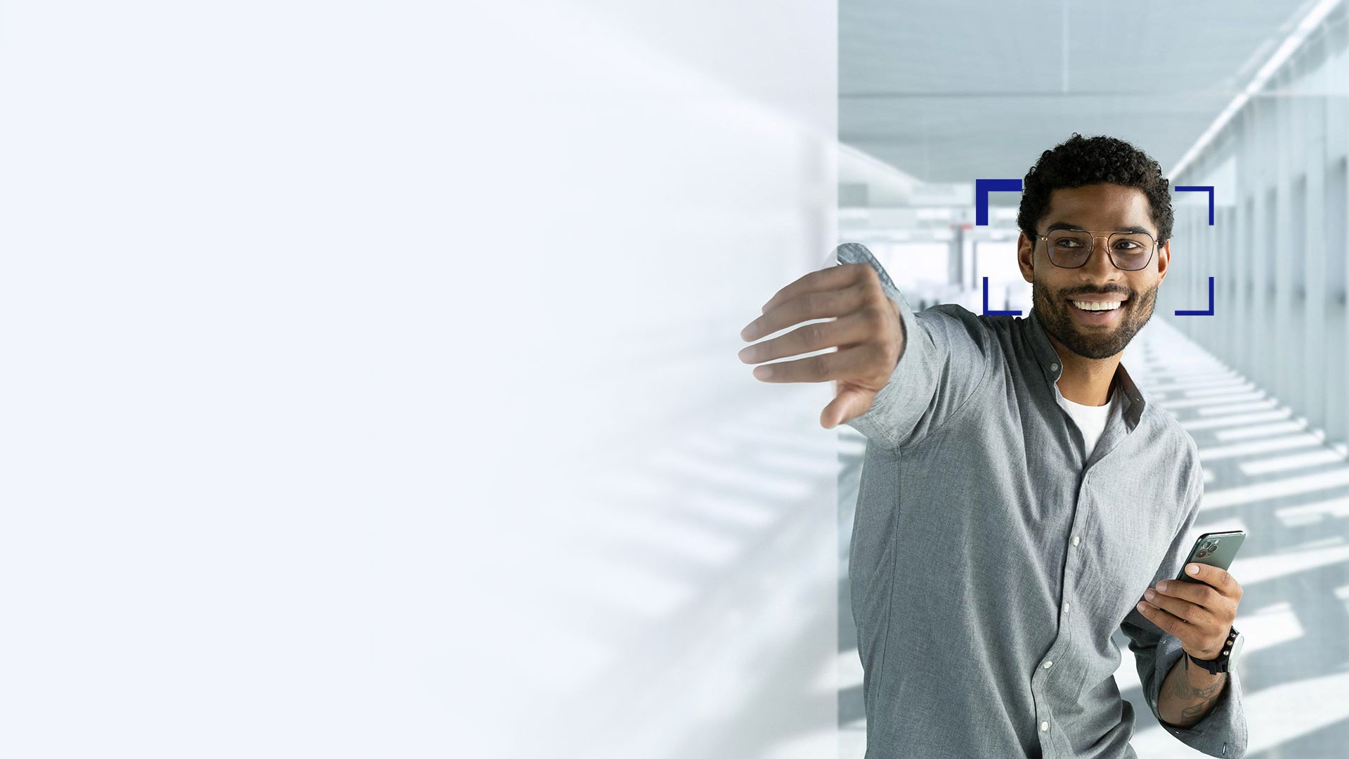 En ung mann med svart hår som smiler og strekker seg med hånden gjennom skjermen iført ZEISS SmartLife-glass.