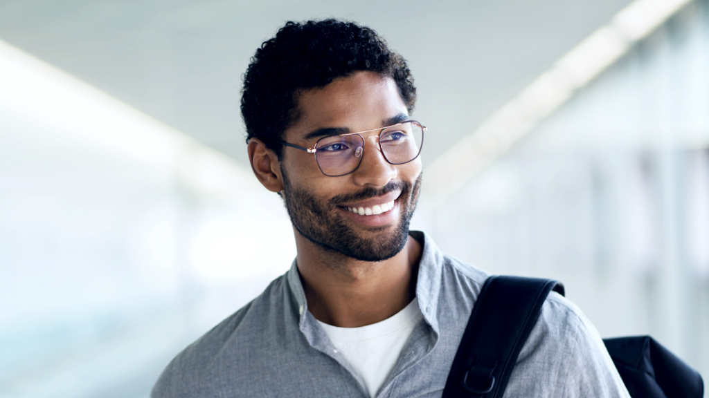 En ung mann som smiler med en ryggsekk over skulderen har på seg ZEISS Digital SmartLife-briller og ser til siden.
