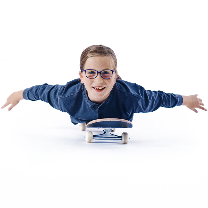 En ung jente med briller ligger flatt på skateboardet.